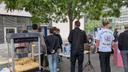Mehrere Personen stehen an einem Stand mit Popcornmaschine und Glücksrad im Freien unter Bäumen