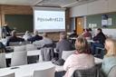 Ein Seminarraum voller Menschen die auf eine Leinwand schauen, auf der ein junger Professor ein Passwort projiziert hat.