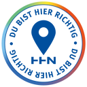 A single-color circular emblem with a thick border in a gradient of blue, green, yellow, and red. A large location pin symbol is centered inside the circle, with the HHN logo below it. The phrase 'DU BIST HIER RICHTIG' is written in uppercase letters along the top and bottom of the inner circle, separated by two small dots.