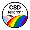 Runder Schriftzug mit dem Text 'CSD Heilbronn' über einem stilisierten Regenbogen und Transgender-Flaggenfarben in einem schwarzen Kreis