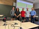 Studierende vor einer Wand, an die per Beamer das Bild einer virtuellen Straßenkreuzung projiziert ist. Im Vordergrund sind Miniaturampeln zu sehen.