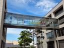 Zu sehen ist ein Bild des verglasten Übergangs zwischen S- und T-Gebäude am Bidungscampus Heilbronn. Das Glas ist großflächig beklebt mit einer Folie. Diese zeigt das Motto der HHN "Du bist hier richtig" sowie das dazu entwickelte Key Visual.