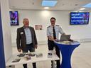 Zwei Polizisten an einem Stand mit Tisch und Stehtisch, im Hintregrund Bildschirme mit "Willkommen beim CyberSecurity Day"