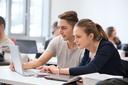 Studierende arbeiten in einem Hörsaal zusammen an einem Laptop.