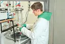 Student im weißen Laborkittel bereitet einen Versuch für einen Filterreaktor vor, der unter einem Laborabzug stattfindet.