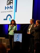 Eine Frau und zwei Männer auf einer BÜhne im Hintergrund eine Präsentation mit den Logos GfA und HHN.