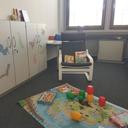 Kinderspielecke mit Spielteppich, bunten Bauklötzen, Kinderbüchern auf einem Stuhl und Schränken mit Tieraufklebern