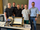 Ein Professor und mehrere Studenten präsentieren eine Maschine. 