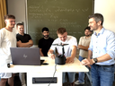 Ein Professor und mehrere Studenten präsentieren eine Maschine. 