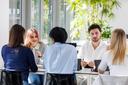 Studierende sitzen um einen Tisch und sprechen miteinander. 
