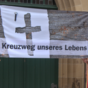 Das Bild zeigt eine weiße Fahne, auf der ein graues Kreuz abgebildet ist.