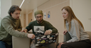 Drei junge, diskutierende Menschen vor einem Laptop mit vielen Stickern drauf.