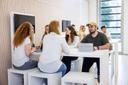 Mehrere Studierenden sitzen mit ihren Tablets an einem Highdesk und unterhalten sich.