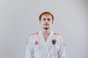 Junger Mann im weißen Karate-Trainingsanzug blickt frontal in die Kamera