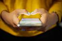 Nahaufnahme von zwei Händen, die ein Smartphone bedienen. Die Person trägt ein gelbes Oberteil und hat hellblau lackierte Fingernägel. Der Bildschirm des Smartphones ist eingeschaltet und zeigt Aktivität.