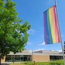 Das Bild zeigt eine gehisste Regenbogenflagge. Im Hintergrund ein Gebäzude des Campus Sontheim.