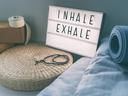 Die Ecke eines Raumes mit Yogablöcken, Kissen und einer Matte sowie ein Schild auf dem "Inhale Exhale" Steht