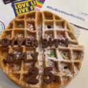Waffel mit Puderzucker, bunten Streuseln und Schokoladenbuchstaben, die "DIVERSITY DAY 25" bilden, auf einem Tisch mit Flyern und Aufklebern.